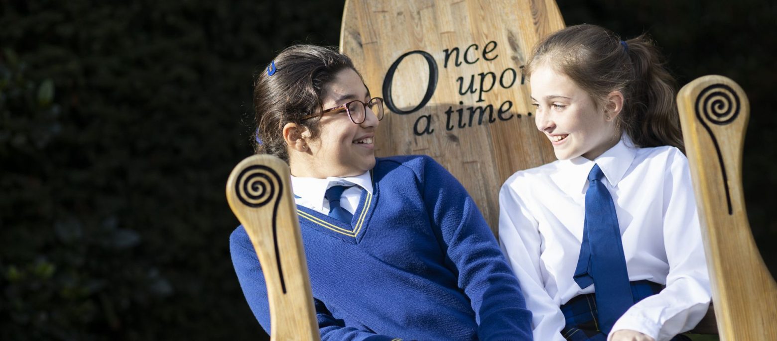 two school girls sitting on a wooden chair with "Once Upon a Time" engraving