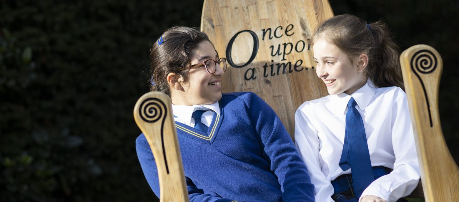 two school girls sitting on a wooden chair with "Once Upon a Time" engraving