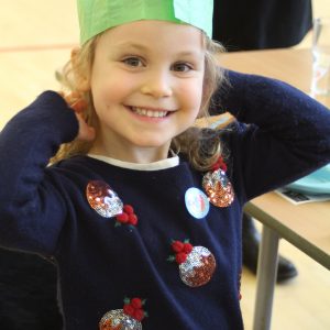 child wearing a Christmas Jumper and a green hat from a cracker