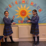 girls standing by a welcome sign